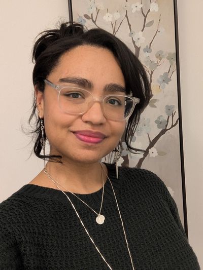 A woman with glasses smiling in front of floral wall art.
