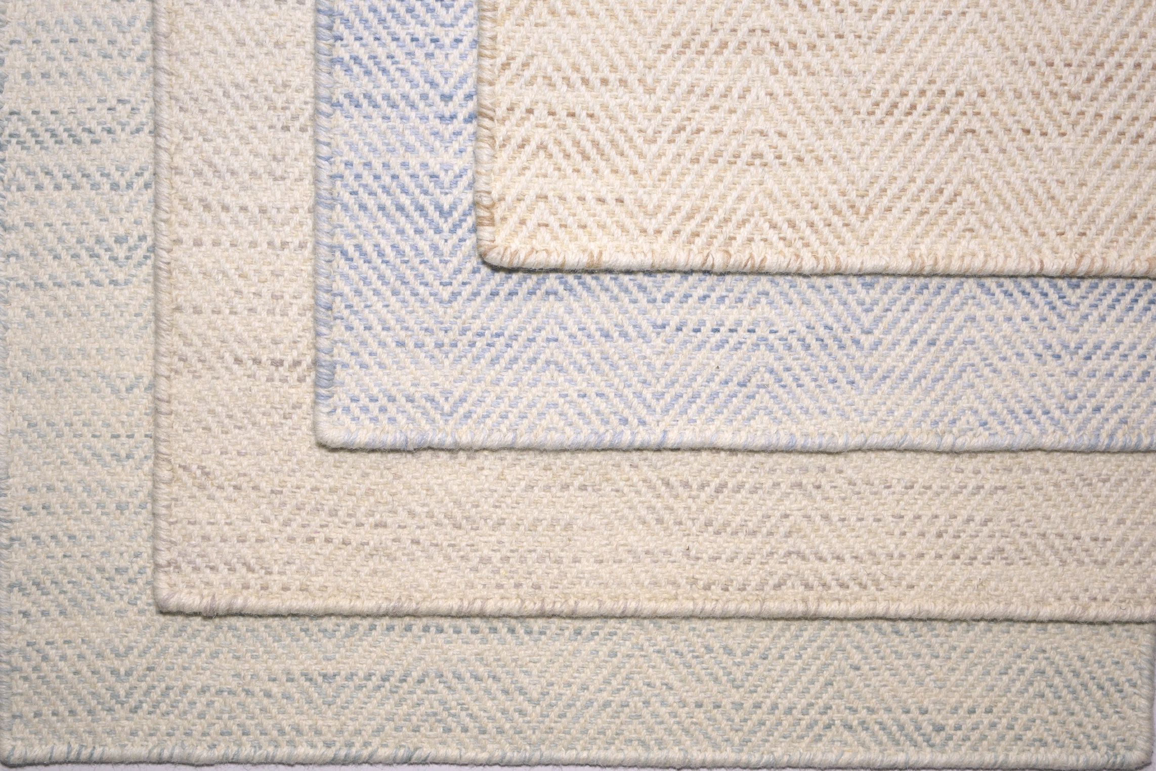 Stack of woven fabric rugs with chevron patterns in light blue and beige.