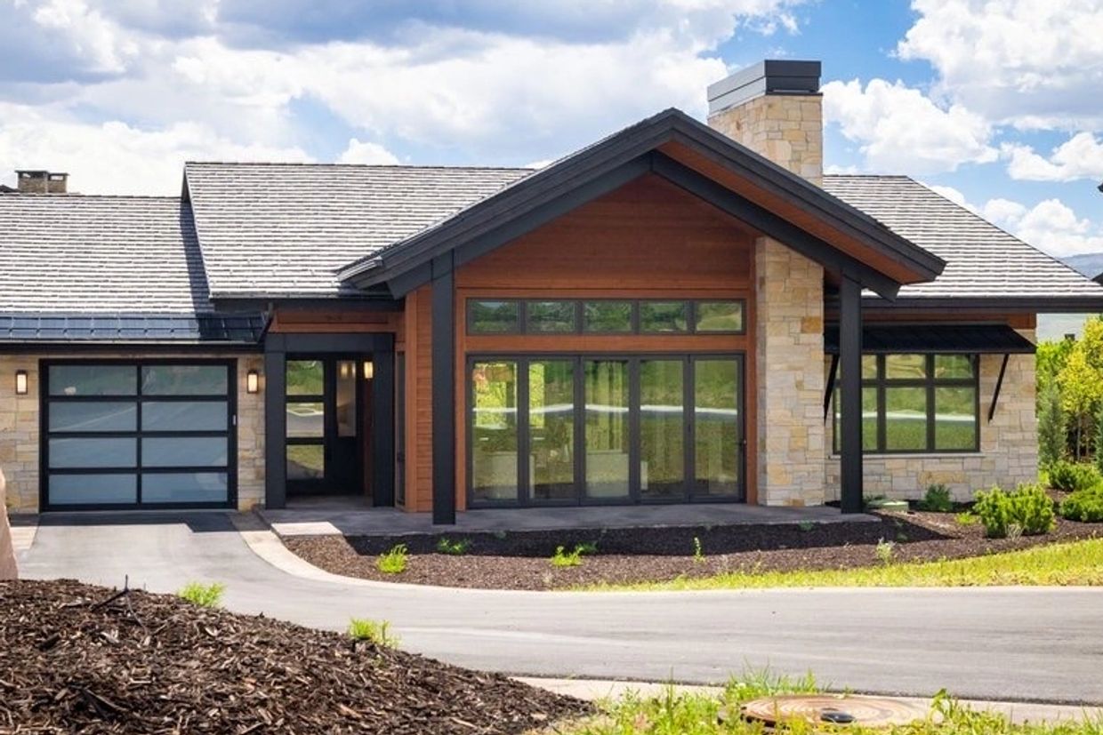 Modern house with large windows and stone chimney under a partly cloudy sky.