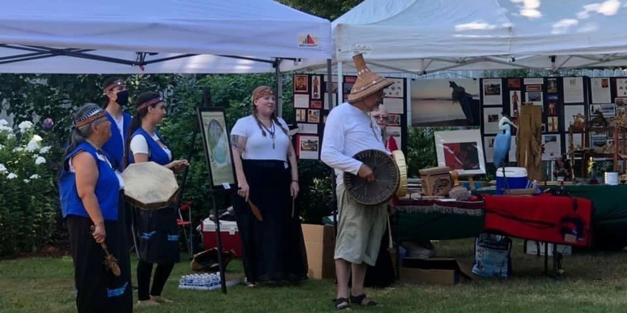 5 Snohomish members holding drums in front of Blue Heron Canoe Family display outside in tent.