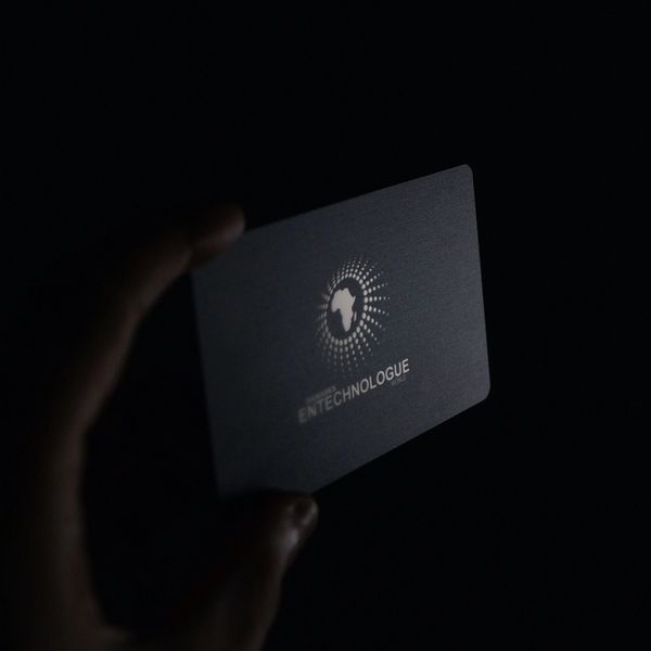 Hand holding a dark card with an African continent logo and EN TECHNOLOGUE text.
