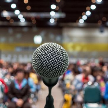 A microphone focused with a blurred audience in the background at an indoor event.