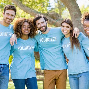 Group of diverse volunteers smiling outdoors in blue T-shirts.