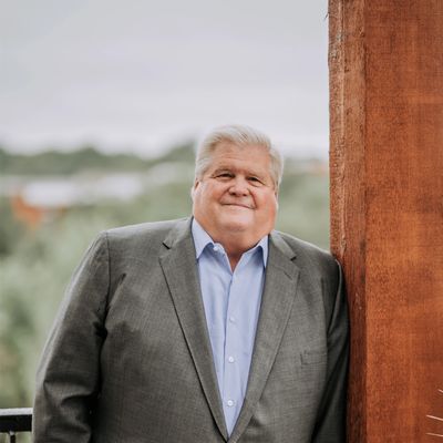 Older man in a suit smiling outdoors.