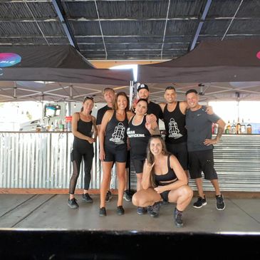 Group of eight people posing together under a canopy, all wearing black workout attire.