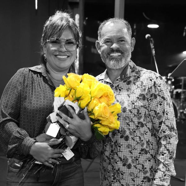 A smiling couple poses with a vibrant bouquet of yellow roses in black-and-white surroundings.
