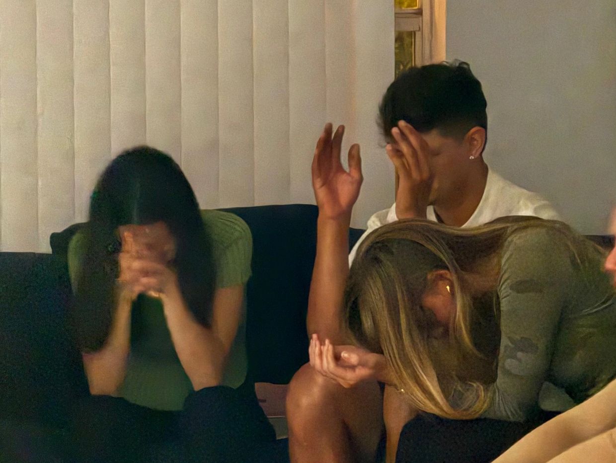 Three people sitting with heads down, appearing upset or distressed indoors.