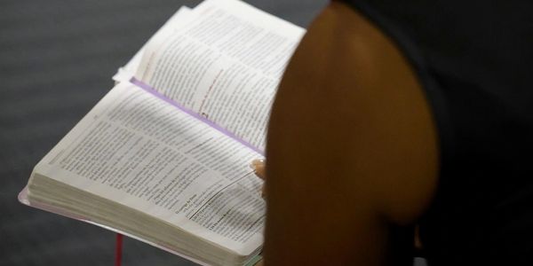 Person reading a book with a purple ribbon bookmark.