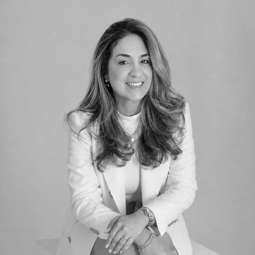Smiling woman in a white blazer sitting.