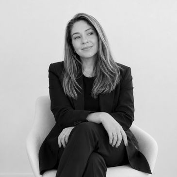 Woman in black outfit sitting on a chair, smiling.