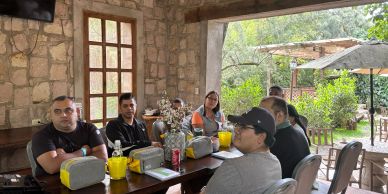 Group of six people sitting around a table indoors near a garden.