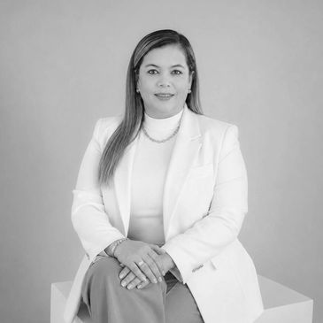 Professional woman in white blazer seated with hands crossed.