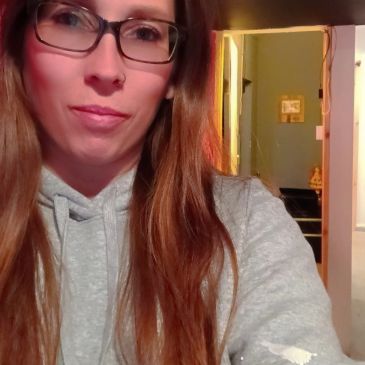 Woman with glasses and long hair in a gray hoodie.