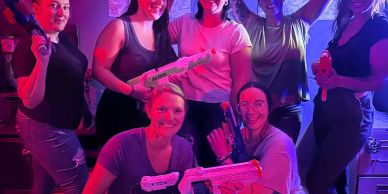 Group of people posing with toy guns under colorful lights.