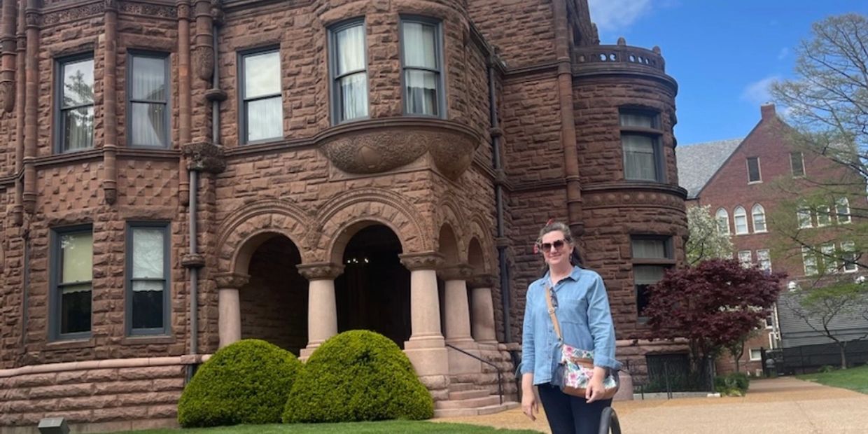 A woman standing in front of a historic stone building on a sunny day.