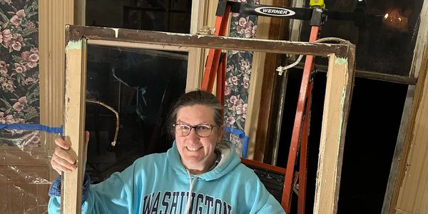 Smiling woman holding an old window frame indoors.