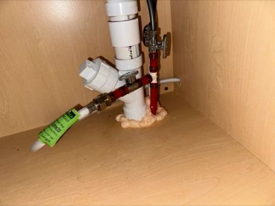Plumbing pipes and valves installed under a wooden cabinet with foam insulation.