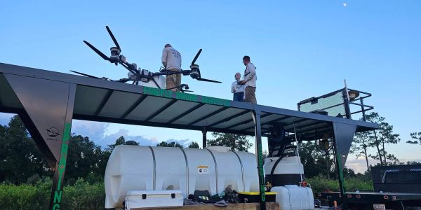 Three people stand on a platform with equipment and tanks around.