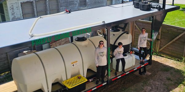 Three people with large tanks under a canopy in a backyard.