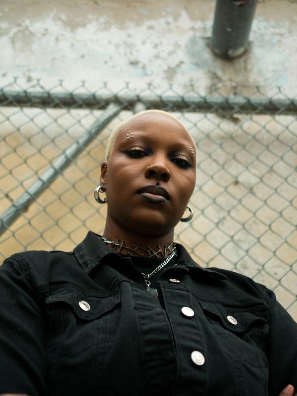 Confident person with piercings and black lipstick against a chain-link fence.