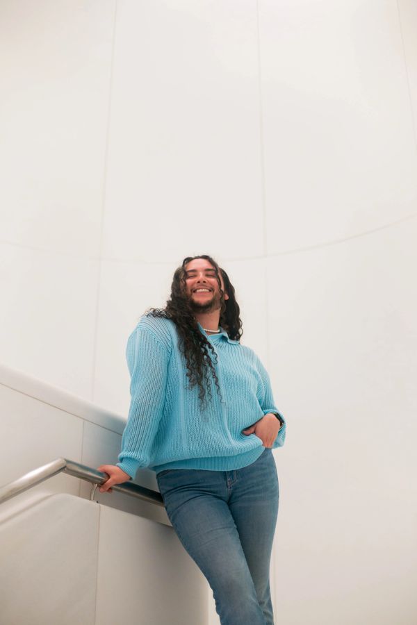 Person smiling and leaning on a handrail wearing a blue sweater and jeans.