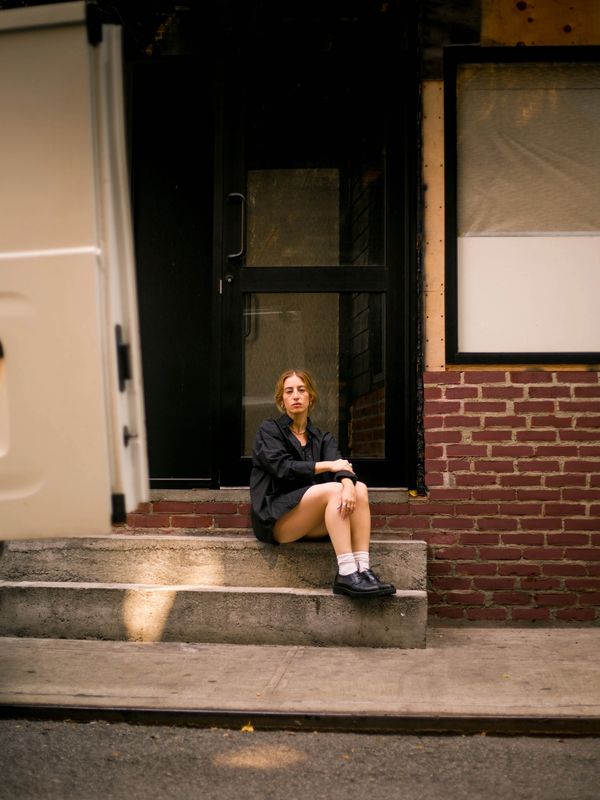 Woman in black sitting on concrete steps outside a brick building.