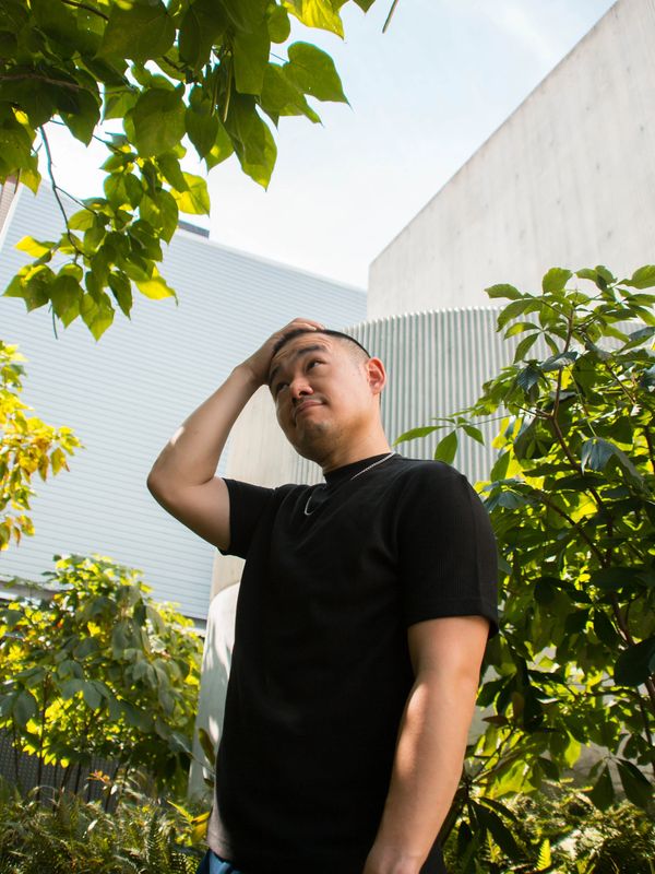Man in black shirt standing thoughtfully among green plants outdoors.
