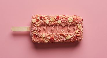 A pink crumb-coated ice cream bar with the word 'YUM!' on a matching pink background.