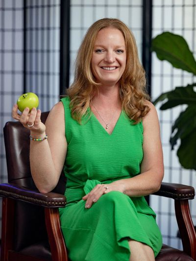 Woman in green dress holding a green apple, smiling.