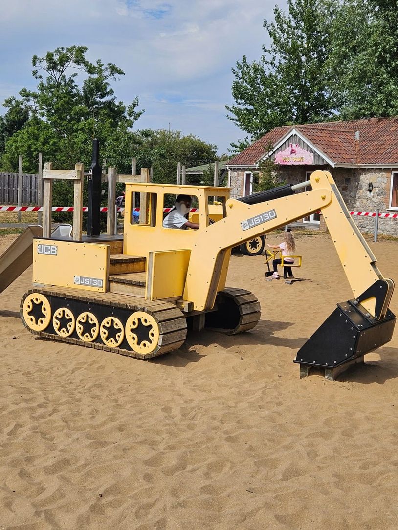Child playing in a yellow excavator toy on sand.