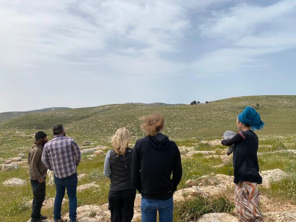 Group of people standing on rocky terrain looking at hills.