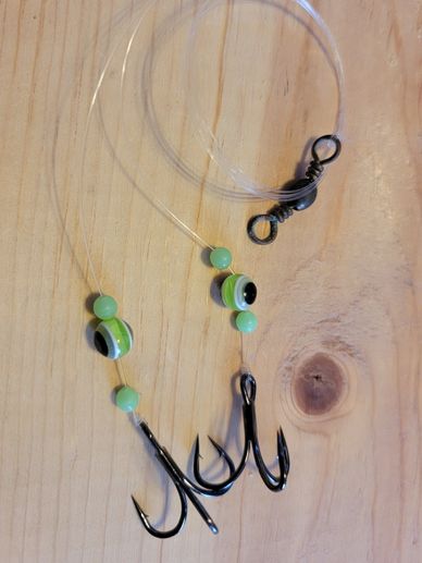 Fishing rig with green beads and treble hooks on a wooden surface.