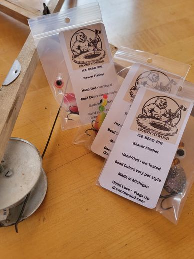 Hand-tied ice fishing bead rigs in clear plastic bags on a wooden table.