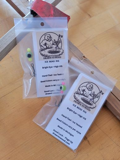 Two packages of Drawn To Wood ice bead rigs on a wooden surface.