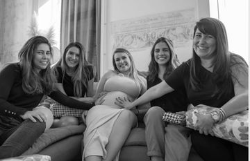 Group of five women smiling, with one pregnant woman in the center.