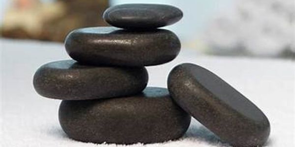 Four smooth black stones stacked on a white surface.