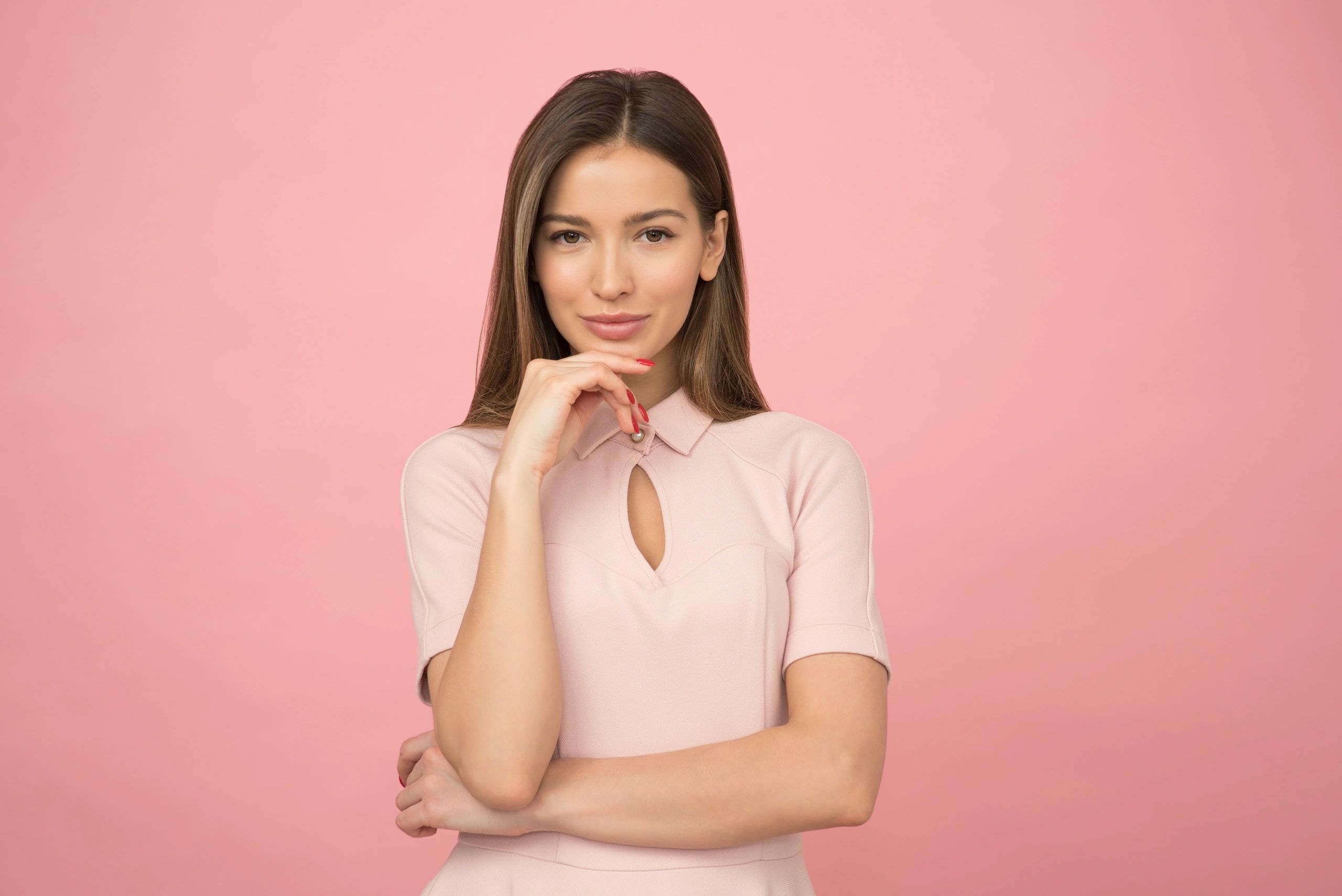 Confident woman posing with hand on chin against pink background.