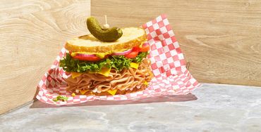 A deli sandwich with lettuce and tomato on checkered paper.