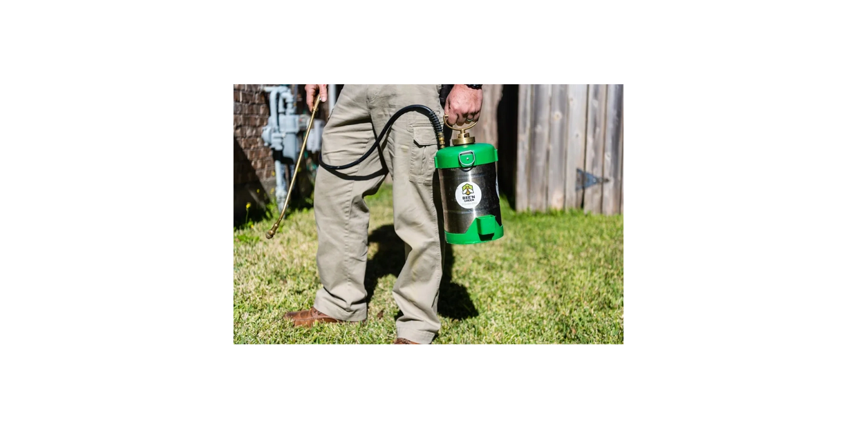 Person spraying lawn with green and silver pesticide sprayer.