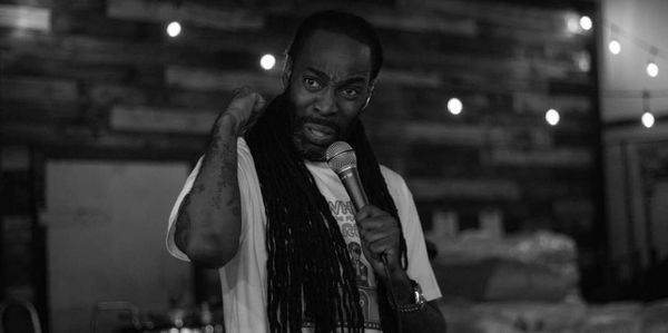 Man with long dreadlocks speaking into a microphone on stage.