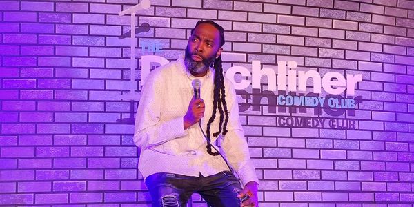 Comedian performing on stage at a comedy club with purple lighting.