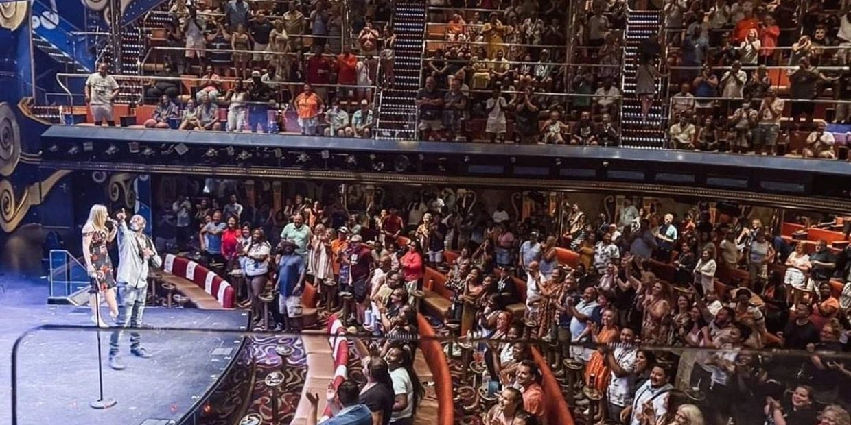 A lively crowd applauds performers on stage in a theater.