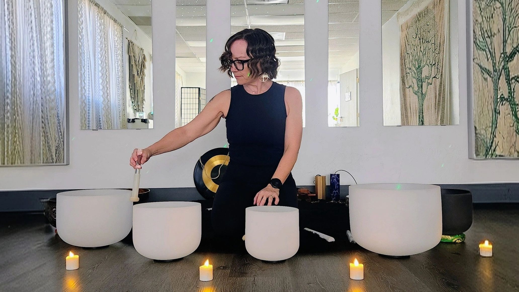 girl playing crystal sound bowls inside a candle lit yoga studio. tall mirrors are in the background