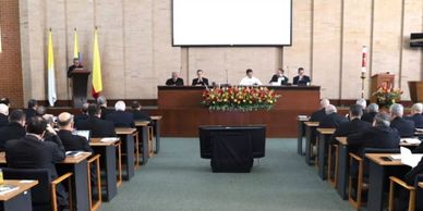 Formal meeting or conference in a large hall with delegates seated and speakers at a podium.