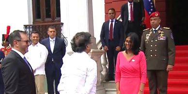 Officials greeting each other outside a government building with Venezuelan flag.