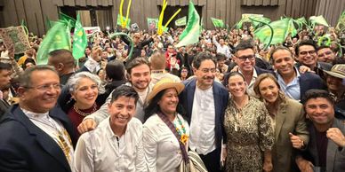A large group of people smiling and holding green flags indoors.