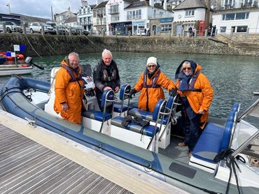 Image: a group of people in orange dry robes onboard the RIB Harbinger in St Mawes Harbour