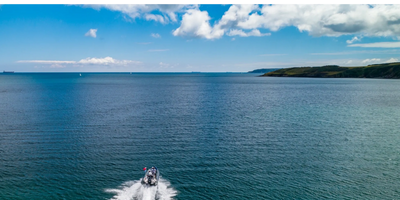 Image: a fast boat on a flat sea heading to the distant horizon near Falmouth, UK