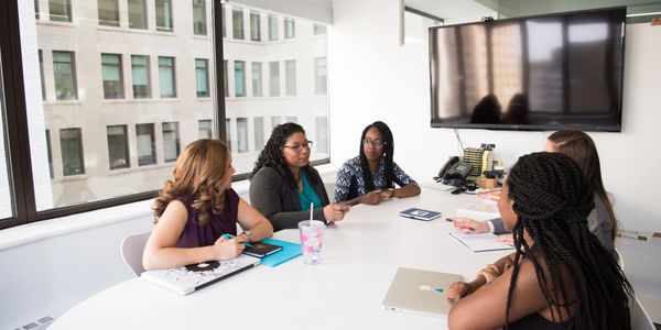 Five women engaged in a meeting around a conference table in an office.