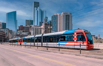 A modern train on an urban track with city buildings in the background.